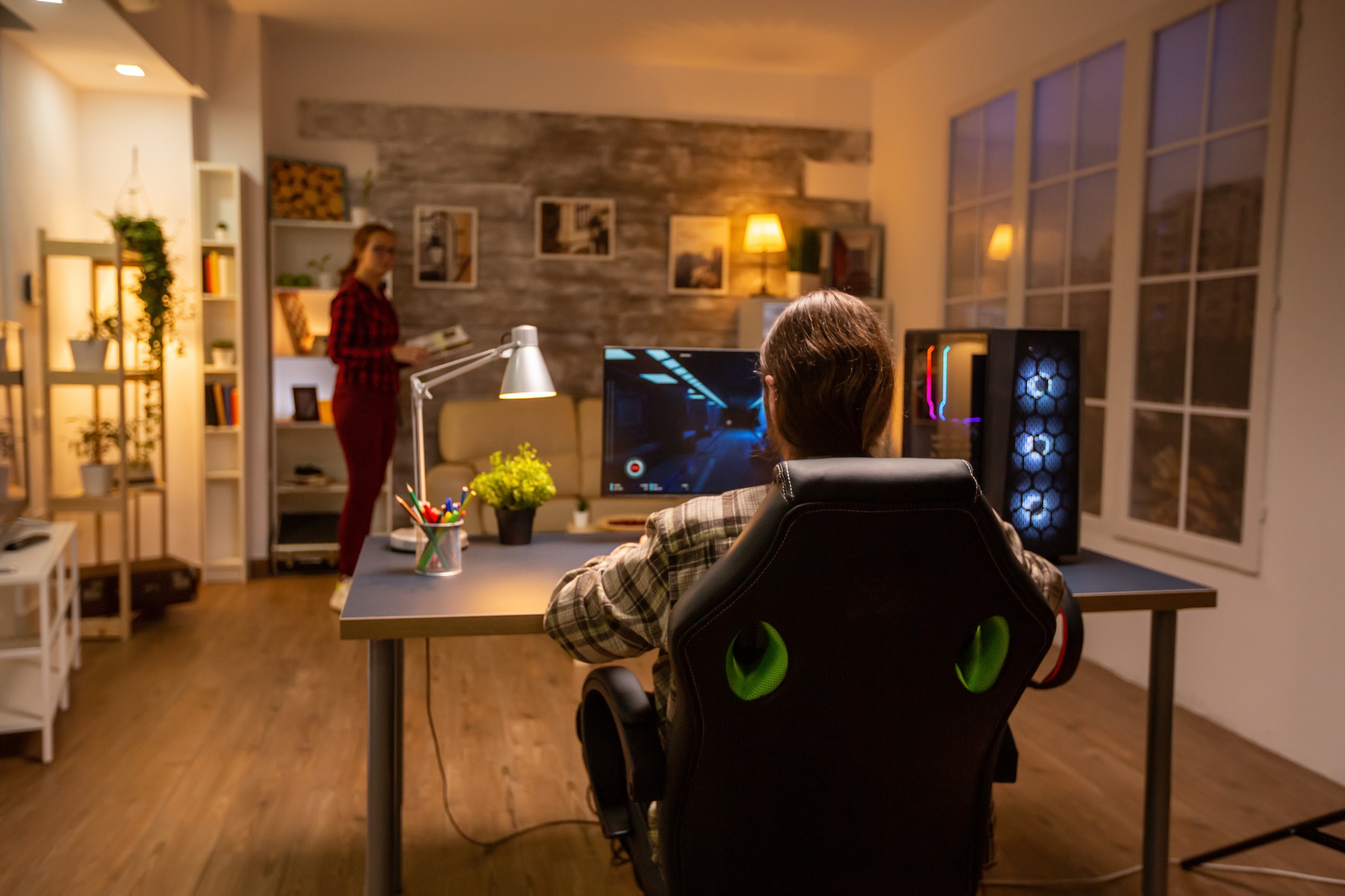 Back view of professional video gamer playing on powerful PC late at night in the living room